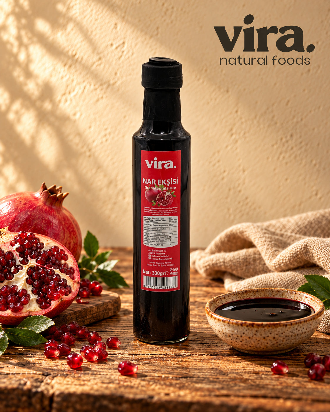 vira. Granatapfelsirup 330g in Glasflasche mit frischen Granatäpfeln und Schälchen Sirup auf Holztisch