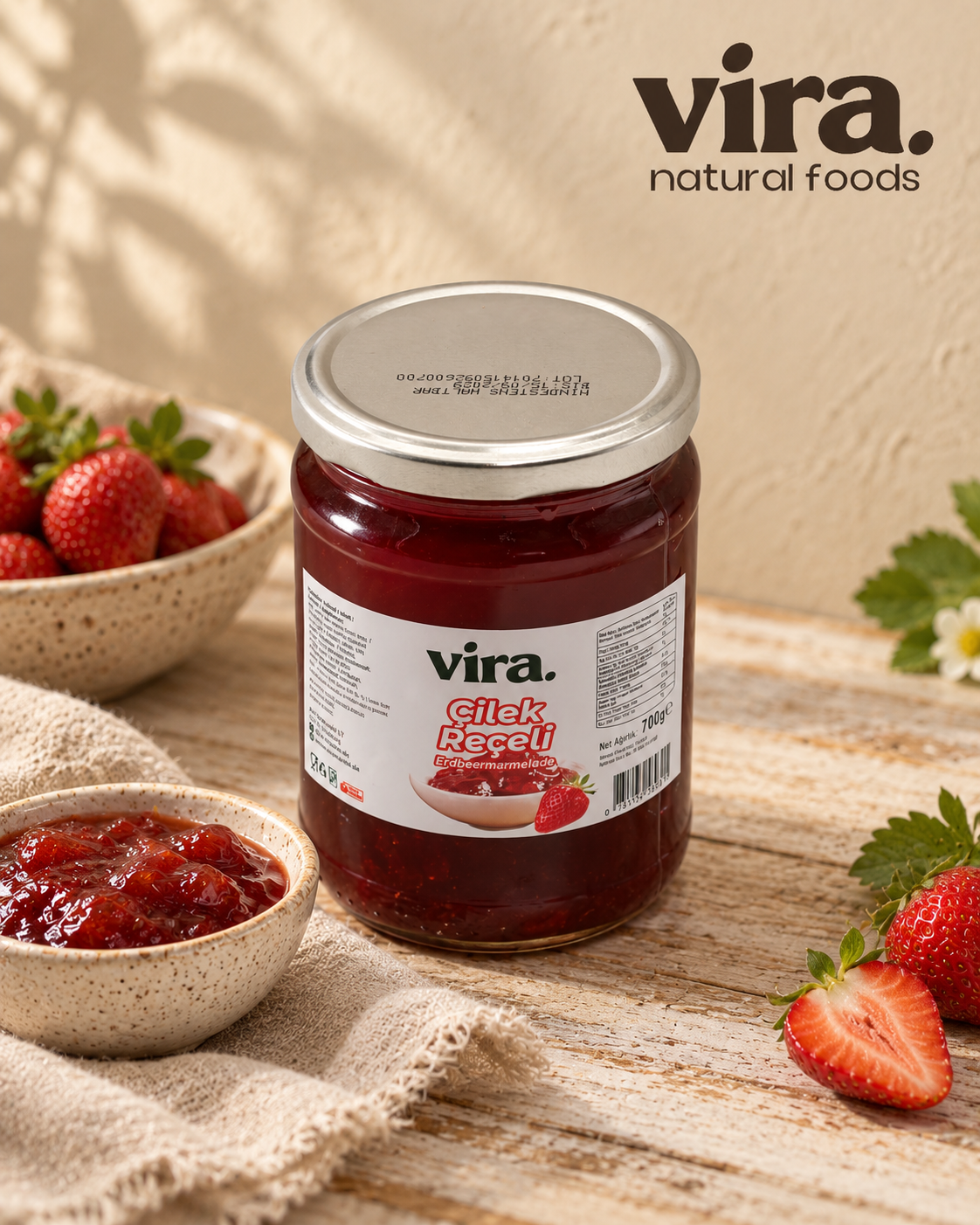 vira. Erdbeermarmelade 700g im Glas mit frischen Erdbeeren und einer Schale Marmelade auf Holztisch