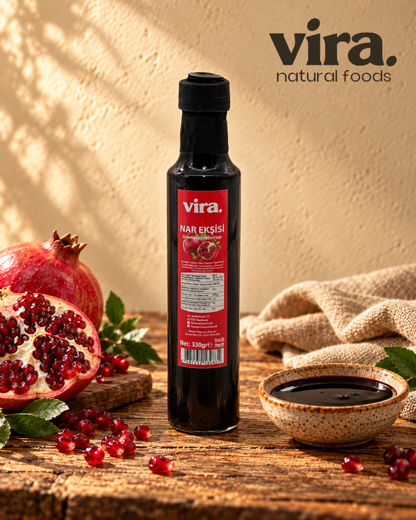 vira. Granatapfelsirup 330g in Glasflasche mit frischen Granatäpfeln und Schälchen Sirup auf Holztisch