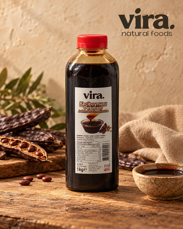 vira. Johannisbrotmelasse 1 kg Flasche mit Johannisbrotschoten und Schale Melasse auf Holztisch